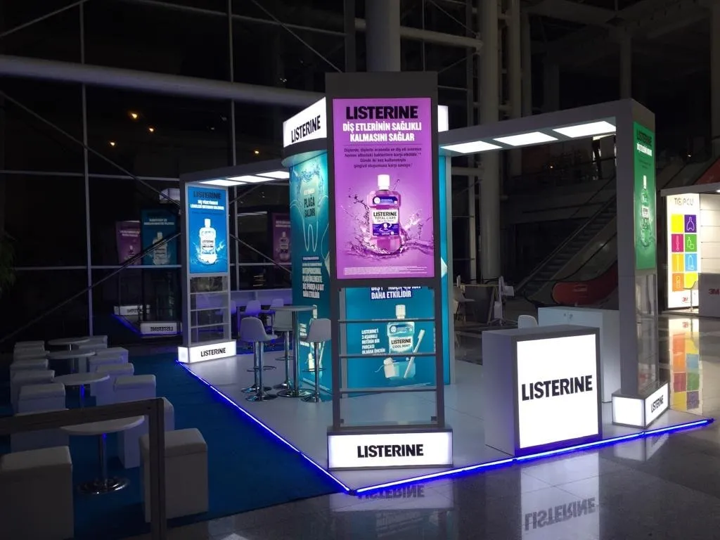 Karanlık salonda ışıklı totem ve vitrinlerden oluşan fuar standı